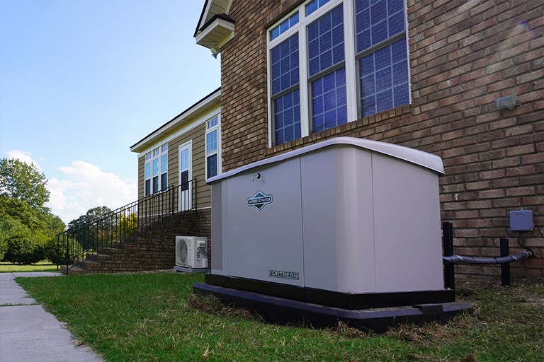 Whole-home generator installed outside a brick home, surrounded by mowed grass.